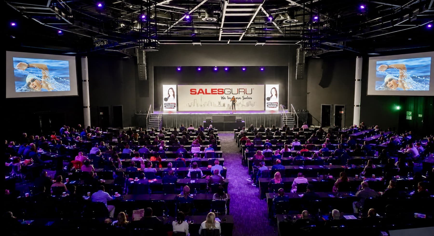 Keynote speaker Carina Bruwer on stage at a large arena conference with a packed audience