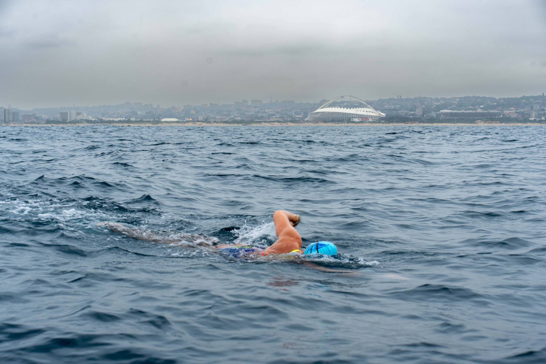 Carina Bruwer swimming in open water with the Moses Mabhida Stadium and the Durban coastline behind her